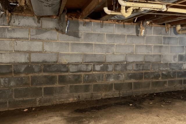 Foundation wall showing signs of moisture and cracking, indicating potential structural issues in a basement, relevant to foundation repair methods and maintenance discussed in the text.