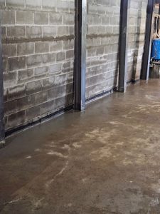 Interior view of a foundation repair site showing concrete walls and a newly poured concrete floor, illustrating underpinning techniques and foundation stabilization methods.
