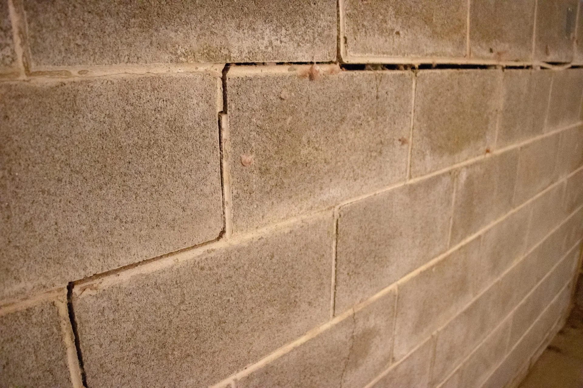 Close-up of a cracked concrete block wall, showing horizontal and vertical fractures. The image conveys a sense of age and structural vulnerability.
