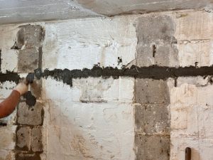 Stair-step cracking in cinder block foundation wall and mortar lines indicating structural stress.